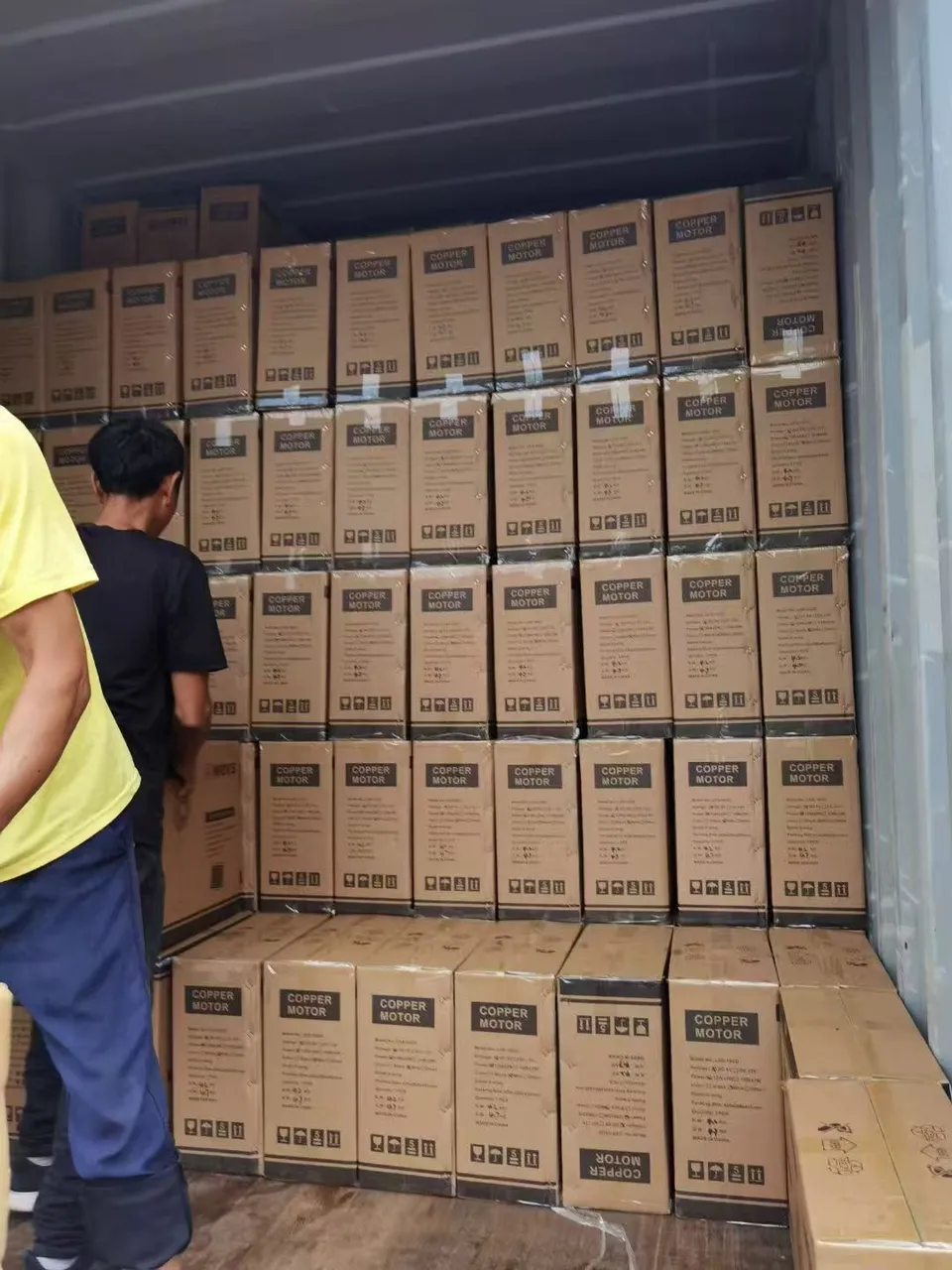 Workers at the doorway of a shipping container with cartons stacked inside.